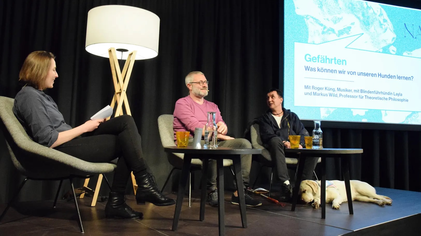 Moderatorin Melanie Pfändler diskutiert mit Professor Markus Wild (Mitte) und Musiker Roger Küng. Dessen Blindenführhündin Layla liegt friedlich zu seinen Füssen.